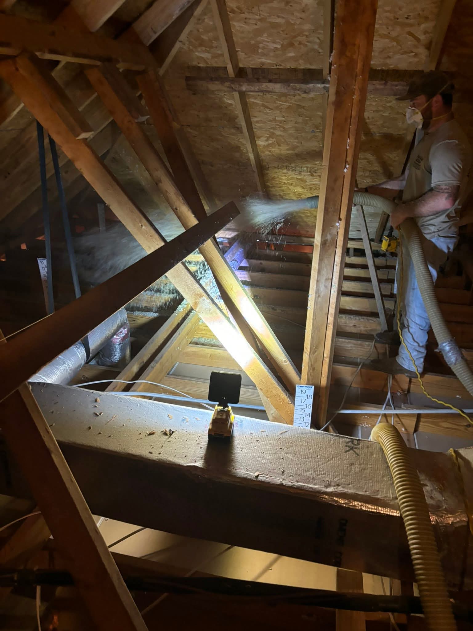 Worker spraying cellulose insulation in attic after removing old dirty insulation